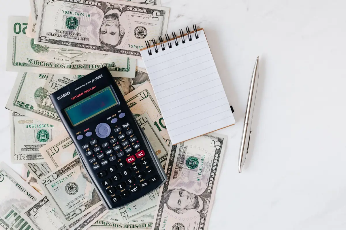 A calculator and a notepad sitting on a stack of paper bills.